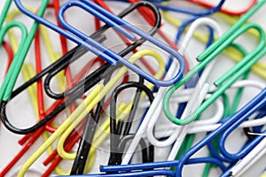 Multicolored colorful paper clips on a white table background close up
