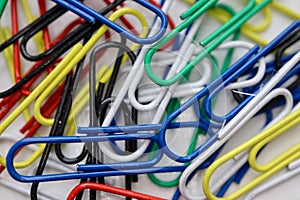 Multicolored colorful paper clips on a white table background close up