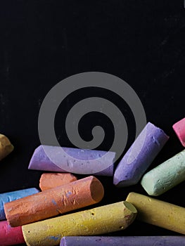 Multicolored crayons lie on a black chalkboard, copy space, macro. The concept of school, education and childhood