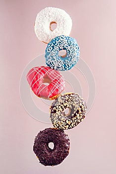 Multicolored decorated doughnuts in motion falling on brown background. Sweet donuts flying in motion.