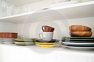 Multicolored dishes on a shelf in a white kitchen cabinet.