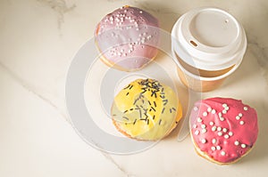 multicolored donuts in glaze and a paper coffee cup /multicolored donuts in glaze and a paper coffee cup on a white marble