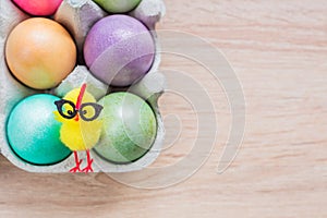 Multicolored easter eggs in a box with cute yellow chick. Top view on wooden background