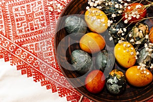 Multicolored Easter eggs in clay bowl on embroidered red towel