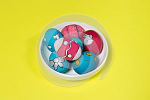 Multicolored Easter eggs in a white plate on a yellow background. Patterns and designs on colored dyed eggs