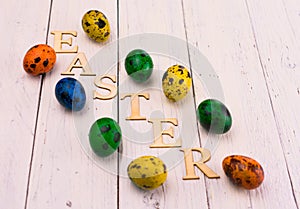 Multicolored Easter quail eggs and the inscription Easter on a white wooden background.