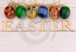 Multicolored Easter quail eggs and the inscription Easter on a white wooden background. Copy space.