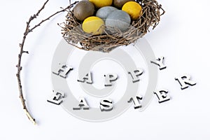 Multicolored eggs in birds nest, branch and the inscription Happy easter on white background