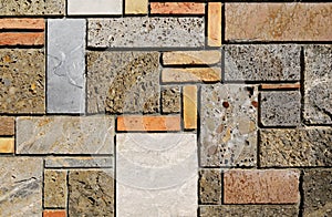 Multicolored external wall made of different types of rocks and bricks arranged geometrically.