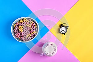 Multicolored fruit loops, jug of milk and alarm clock against the geometric background photo