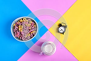 Multicolored fruit loops, jug of milk and alarm clock against the geometric background