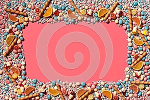 Multicolored glazed dragees and other sweets are arranged in the form of a frame on a coral background.