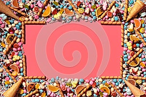 Multicolored glazed dragees and other sweets are arranged in the form of a frame on a coral background.