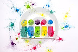 Multicolored holi paints in a palette on a white background from above.