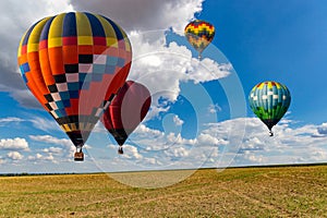 Multicolored hot air balloons fly in blue sky with white clouds over green field