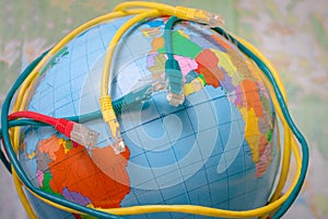 Multicolored internet wires wound around a globe. Connecting server patch cords are on top of the world map. The Internet network