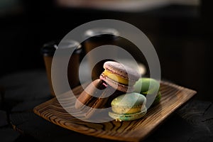 Multicolored macaroons in a wooden plate on the background of two cups of coffee in dark colors