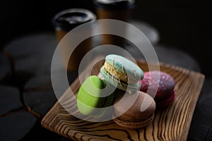 Multicolored macaroons in a wooden plate on the background of two cups of coffee in dark colors