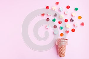 Multicolored Marshmallows and jelly candy out of ice cream cone on pink background