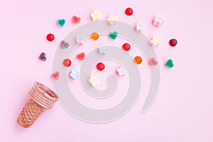 Multicolored Marshmallows and jelly candy out of ice cream cone on pink background