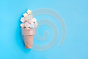 Multicolored Marshmallows out of ice cream cone on blue background