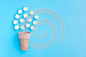 Multicolored Marshmallows out of ice cream cone on blue background