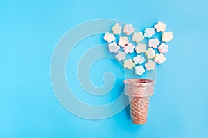 Multicolored Marshmallows out of ice cream cone on blue background