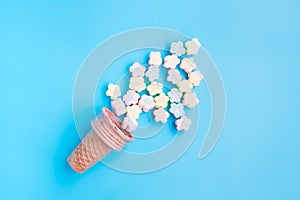 Multicolored Marshmallows out of ice cream cone on blue background