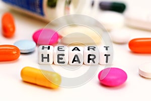 Multicolored medical drugs and letter cubes spelling heart, suggesting cardiac problems