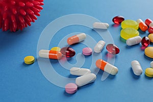 Multicolored medical pills of various shapes and imitation of a coronavirus cell on a blue background