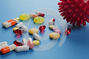 Multicolored medical pills of various shapes and imitation of a coronavirus cell on a blue background