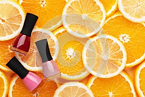 Multicolored nail polishes on a citrus background top view. Tools for professional manicure and pedicure pink and red on oranges