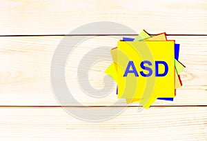 Multicolored office paper stickers with the text ASD Autism Spectrum Disorder on a wooden background. copy space