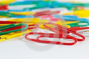 Multicolored office paperclips on white desktop closeup