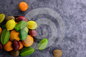 Multicolored organic fruitage on ceramic plate on gray concrete background