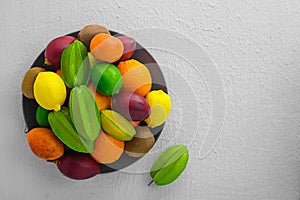 Multicolored organic fruitage on ceramic plate on white concrete background