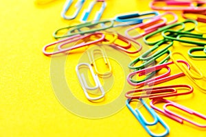 Multicolored paper clips scattered on bright yellow background. School office supplies paperwork documents organization stationery