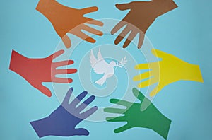 Multicolored paper hands reach for a paper pigeon on a blue background. World Peace Day. World Science Day for Peace and