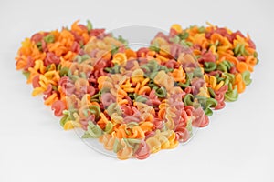 Multicolored pasta scattered on a white background in the shape of a heart. Top view. Copy, empty space for text