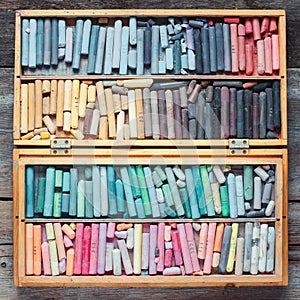 Multicolored pastel crayons in wooden artist box on table.