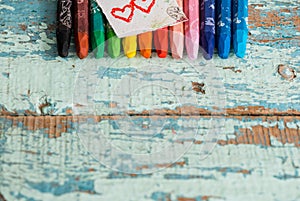 Multicolored pencils like a rainbow on Valentine`s Day on a wooden table. Two red hearts on paper. Copy space, top view