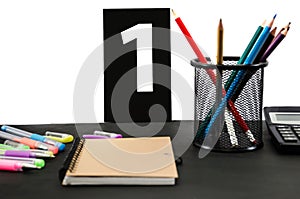 Multicolored pencils, pens, notebook, book and pictures with numbers on a black table. Education concept. Office supplies on the t