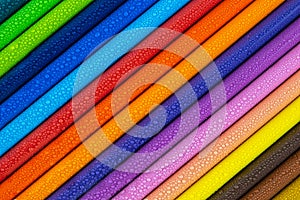 Multicolored pencils with water drops on wooden table