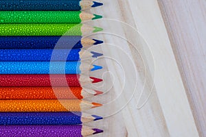 Multicolored pencils with water drops on wooden table