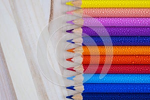 Multicolored pencils with water drops on wooden table