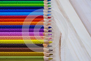 Multicolored pencils with water drops on wooden table