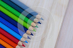 Multicolored pencils with water drops on wooden table
