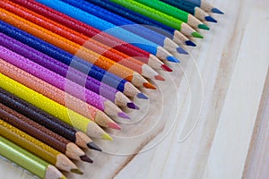 Multicolored pencils with water drops on wooden table