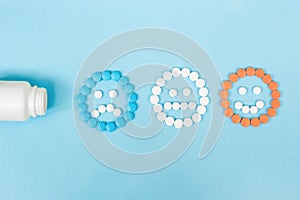 Multicolored pills and funny faces and a plastic bottle on a blue background. The concept of antidepressants and healing