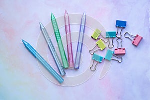 Multicolored plastic crayons and paper-clips from top view on pastel watercolor background.